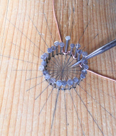 Winding copper wire around the nails in a pattern.