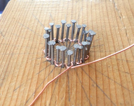 Winding copper wire around the nails in a pattern.