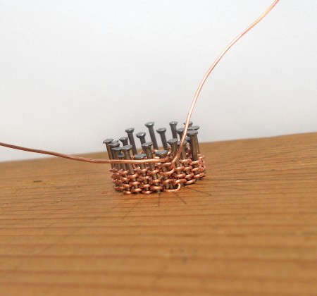 Winding copper wire around the nails in a pattern.