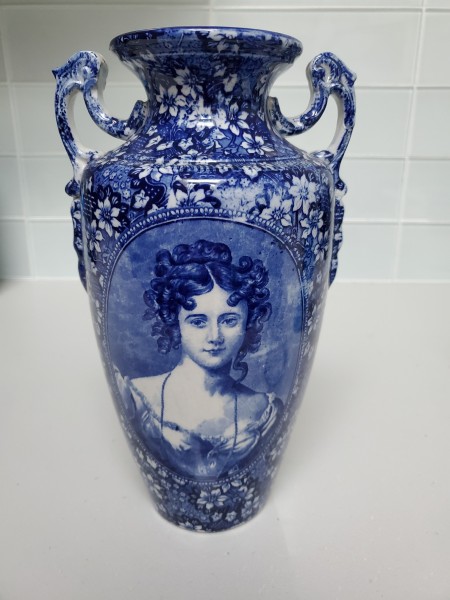 A blue and white vase with an old fashioned ladies face.