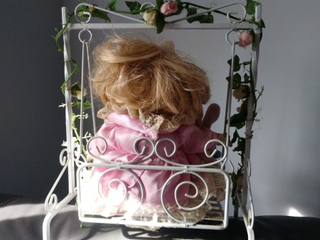 The back of a porcelain doll on a swing.