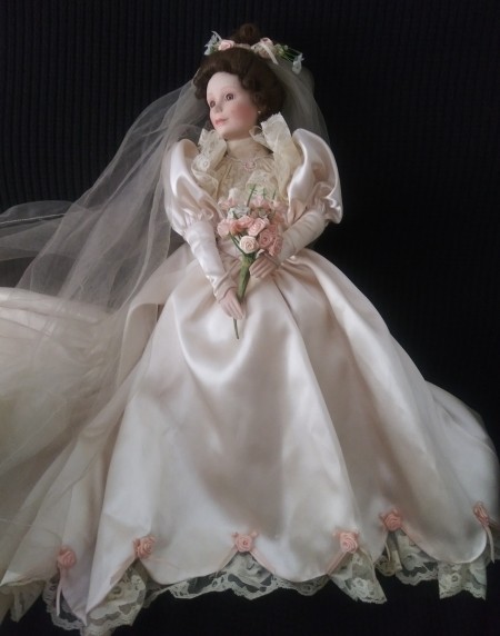 A doll dressed as a bride with a floral bouquet and veil.