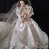 A doll dressed as a bride with a floral bouquet and veil.