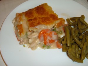 A piece of chicken pot pie on a plate next to cooked green beans.