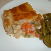 A piece of chicken pot pie on a plate next to cooked green beans.