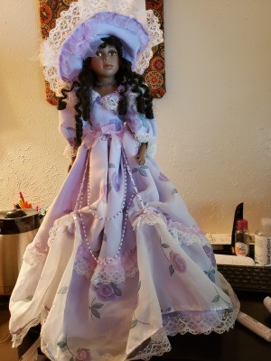 A porcelain doll with dark hair and a fancy lavender outfit.