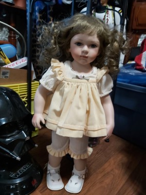 A young girl porcelain doll with light brown hair.