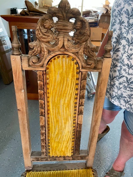 The back of a wooden chair with yellow velvet.