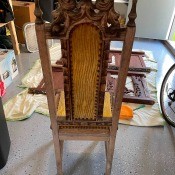 The back of a wooden chair with yellow velvet.