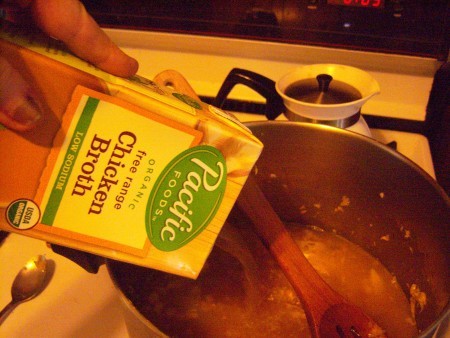 Adding chicken broth to the soup pot.