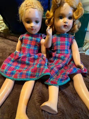 Two old dolls wearing matching dresses.