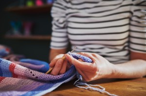 A woman sewing an edge on a blanket.