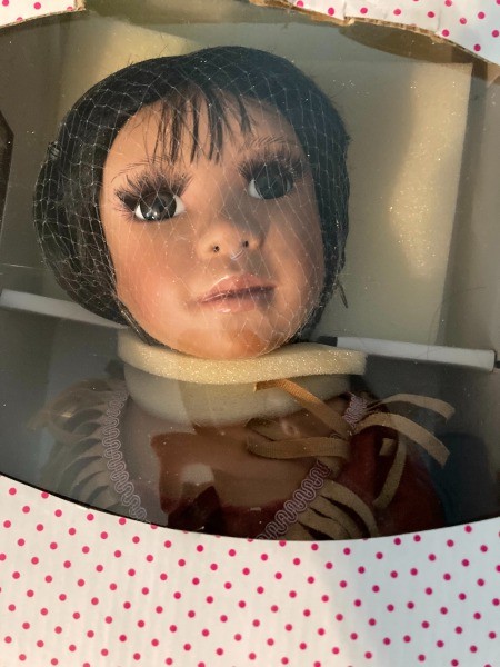 A dark haired porcelain doll in a box.