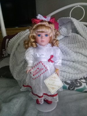 A porcelain doll in a white dress with red trimmings.