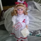 A porcelain doll in a white dress with red trimmings.