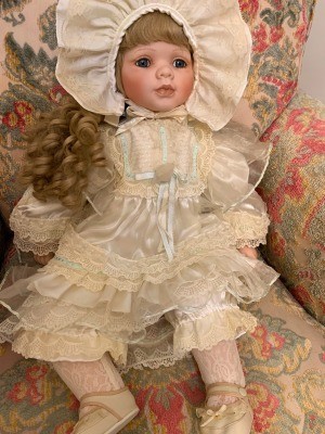 A porcelain doll in a cream colored outfit.