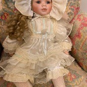 A porcelain doll in a cream colored outfit.