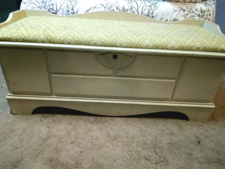A light colored cedar chest with a cushion on top.