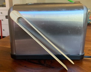 A pair of wooden tongs next to a toaster.