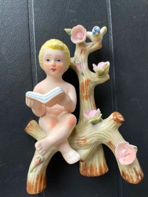 A figurine of a small child reading a book on a flowering branch.