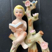 A figurine of a small child reading a book on a flowering branch.