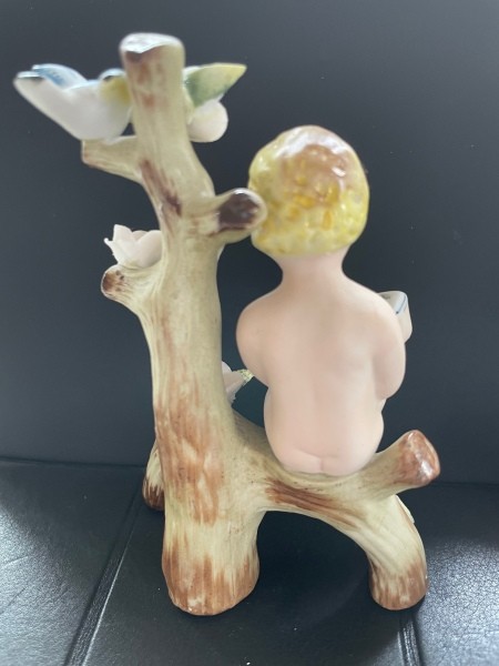The back of a figurine of a small child reading a book on a flowering branch.