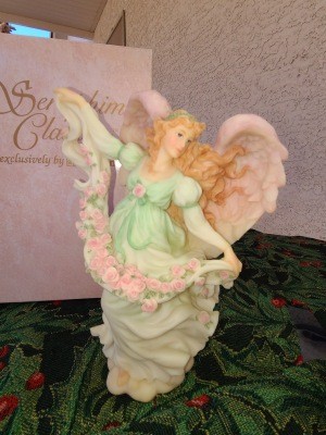 An angel figurine holding a garland of pink flowers.