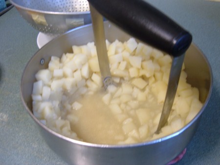 Mashing the cooked potatoes in the pan.