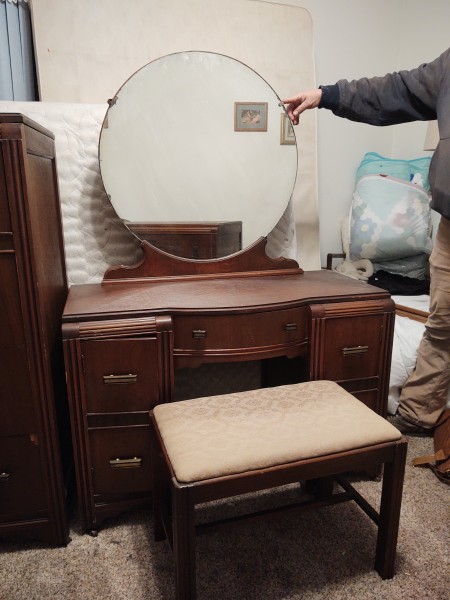 A dresser with round mirror and bench.