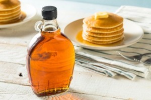 A bottle of maple syrup next to a stack of pancakes.
