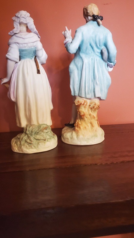 The backs of two figurines dressed in old fashioned clothing.