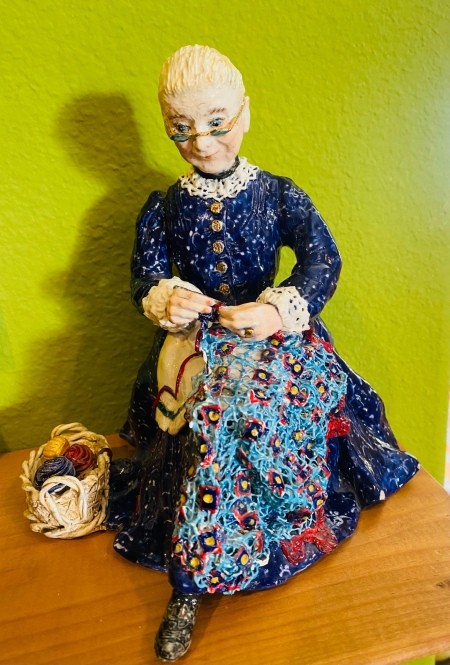 A figurine of a woman making a yarn craft.