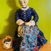 A figurine of a woman making a yarn craft.