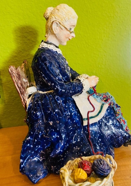 A figurine of a woman making a yarn craft.