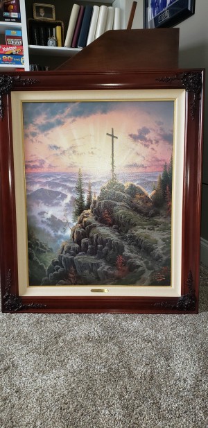 A framed print of Thomas Kinkade's "Sunrise".