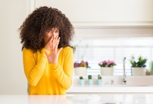 A woman smelling a rotten odor in the kitchen.