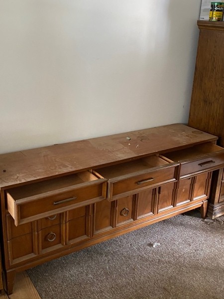 A long wooden dresser with the top drawers open.