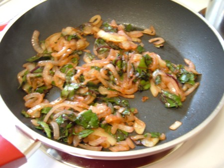 Stir frying beet greens and onions in a pan.
