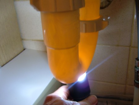 A flashlight being shone on the underside of a plastic drain pipe.
