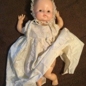 A vintage baby doll in a white gown and bonnet.