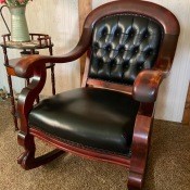 A wooden rocking chair upholstered in black leather.