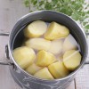 Peeled and halved potatoes in a pot of water.