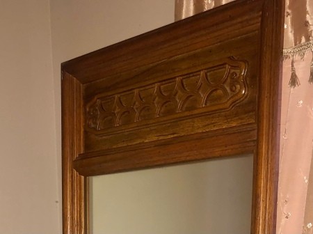 The decorative top of a wooden mirror.