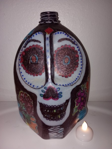 A painted milk jug to resemble a sugar skull, next to a battery operated candle.