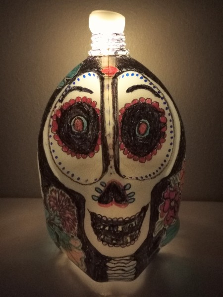 A painted milk jug to resemble a sugar skull, with a candle at the top.