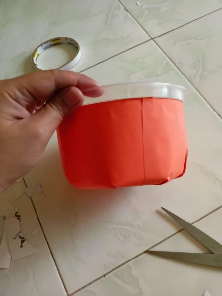 Covering plastic container with orange paper.