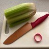 A cutting board with a knife, rubber band and a bunch of celery.