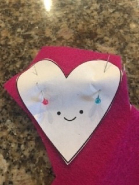 Attaching a heart template to pink fabric.