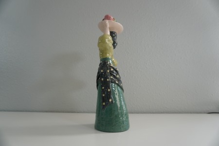 A figurine of a woman carrying fruit on her head, side view.