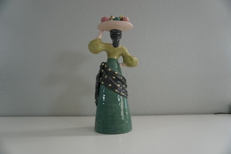 A figurine of a woman carrying fruit on her head, back view.